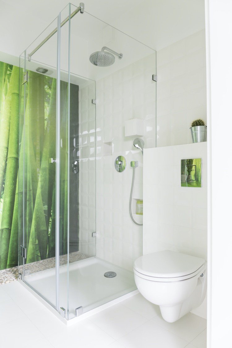 O fotomural chuveiro de vidro de bambu, azulejos brancos e vaso sanitário montado na parede com cisterna embutida fazem o banheiro parecer grande