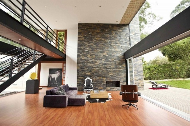 sala de estar com teto alto, parede de pedra, piso de madeira