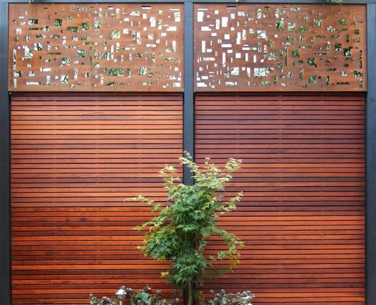 Cerca de segurança minimalista feita de tiras de madeira avermelhadas e detalhes em aço corten