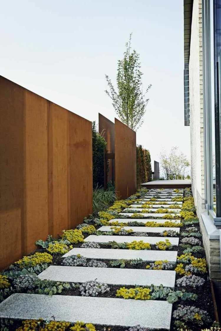 Tela de privacidade de aço corten feita de painéis simples ao longo de um caminho de jardim feito de lajes de pedra