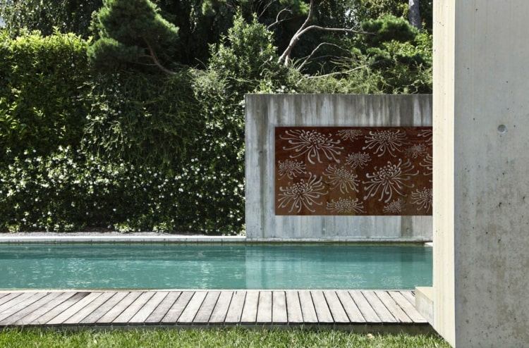 Projeto minimalista do jardim na piscina com telas de privacidade de aço Corten emolduradas em concreto aparente