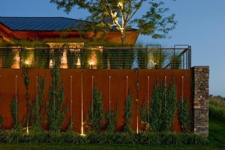 Cerca de alta privacidade com plantas e iluminação em uma parede de pedra