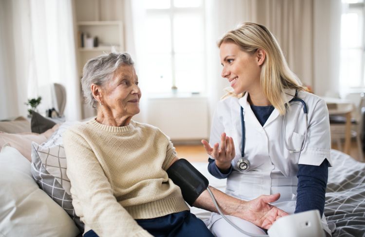 Cuidador fala com a mulher enquanto mede a pressão arterial