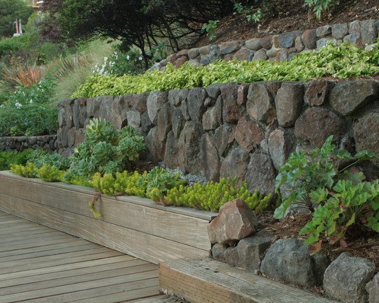 As paredes do jardim são fechadas em pedra natural e deck de madeira
