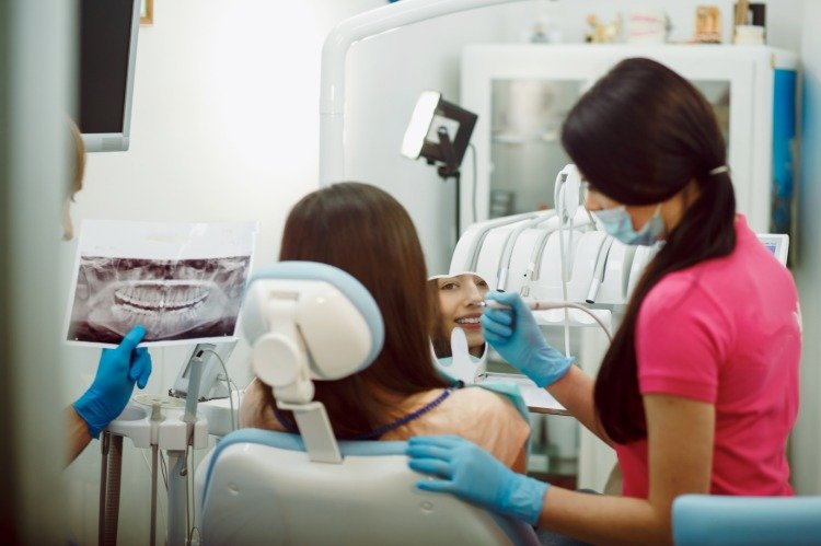 jovem sorridente se olha no espelho enquanto está sentada na cadeira do dentista durante o tratamento