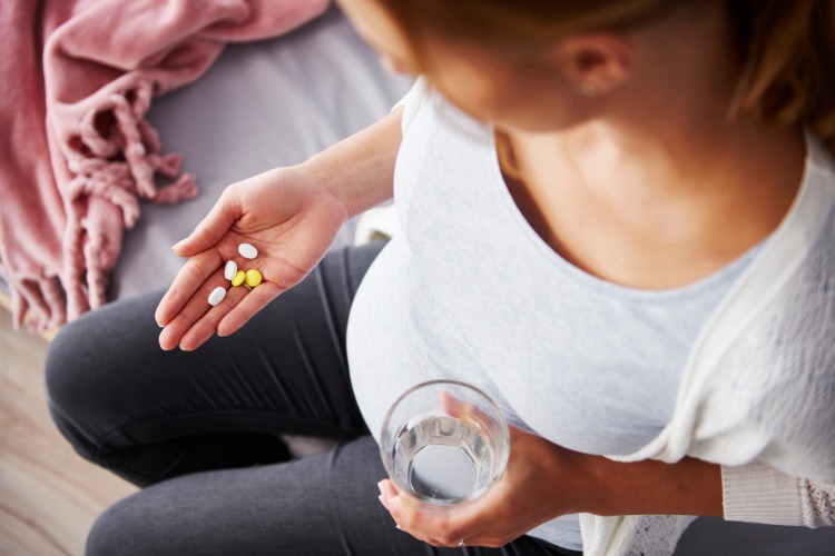 mulher grávida toma suplementos nutricionais com um copo de água