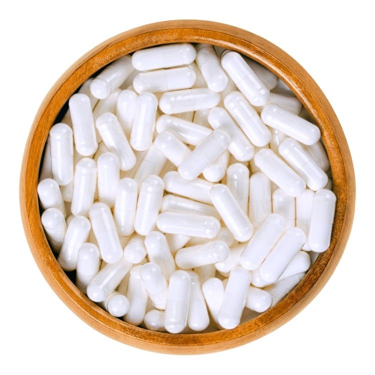 cápsulas brancas como suplemento ao complexo de vitamina b em uma tigela de madeira