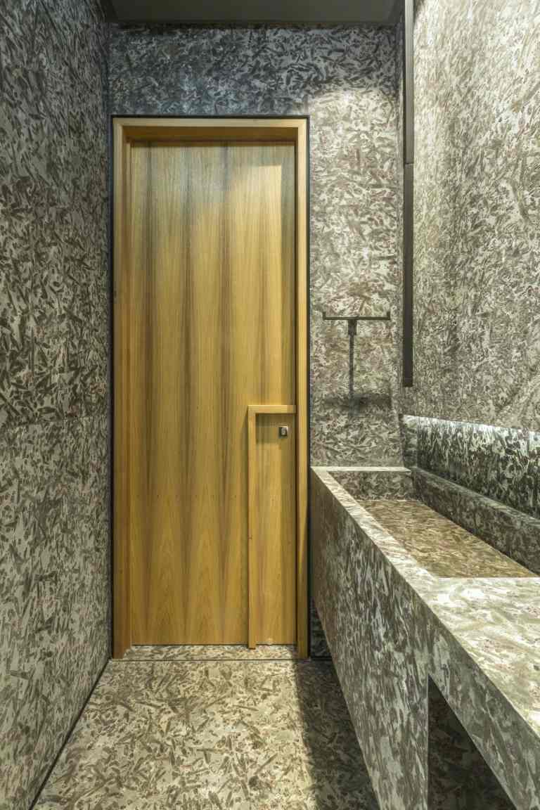 Banheiro em cinza com porta de madeira como destaque de cor e pia embutida