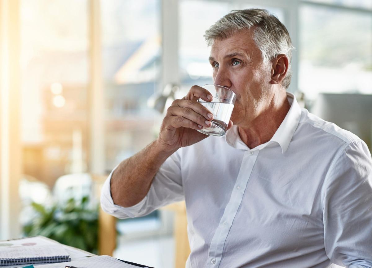 Homem idoso com cabelos grisalhos bebe água de copo para melhor absorção de água e se livrar da barriga de cerveja
