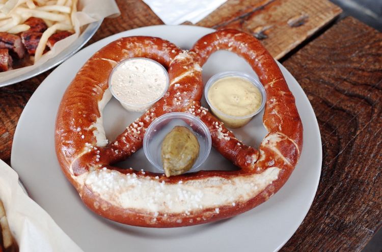 caneca de pretzel grande com molho de coquetel de mostarda prato branco mesa de madeira lanches para festas