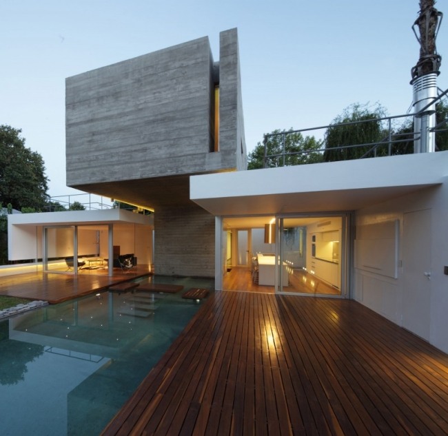 Casa com iluminação flutuante em cantilever e terraço de madeira com pedras para pisar piscina de água