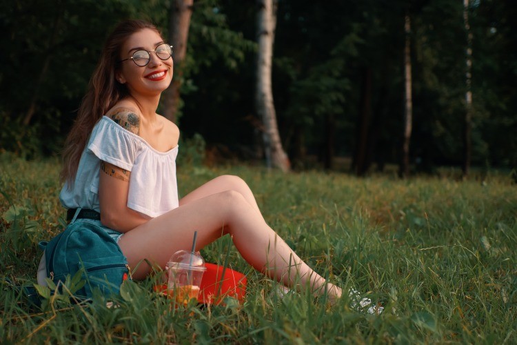 garota sorridente sentada na grama na natureza sob o sol
