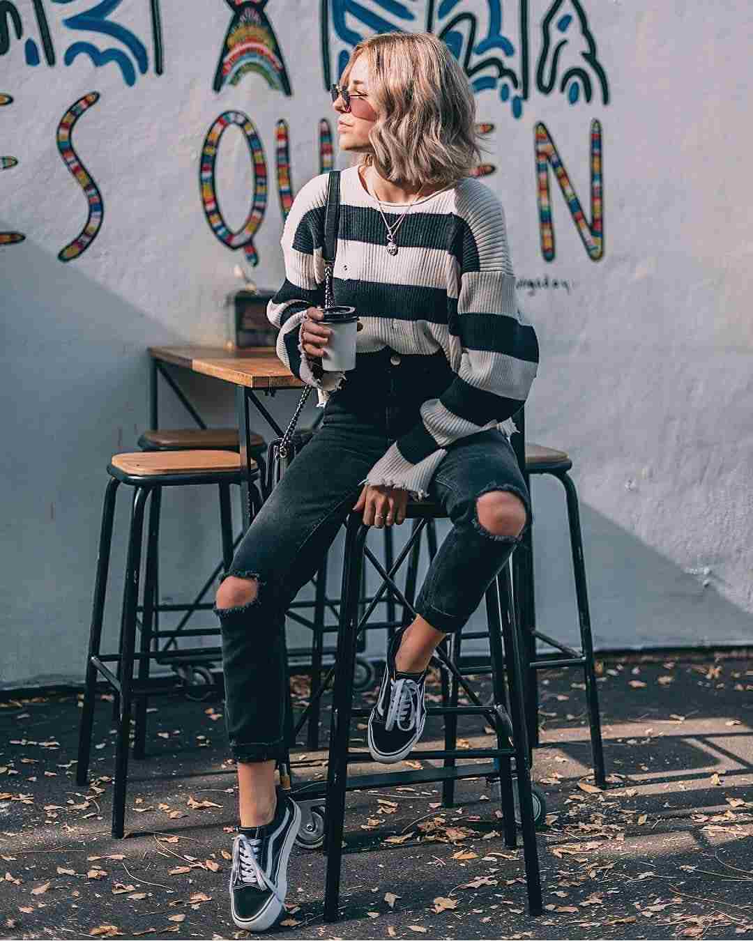A calça jeans da mamãe combina suéter de malha preta com tênis de tamanho grande, cabelo loiro escuro, tendências da moda 2019