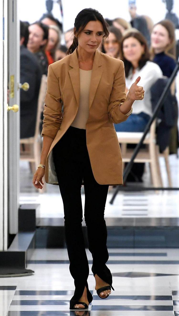 Victoria Beckham com calças pretas divididas e um blazer marrom grande