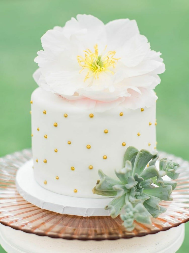 Bolo de casamento branco decorado com pérolas douradas e uma grande flor e planta suculenta