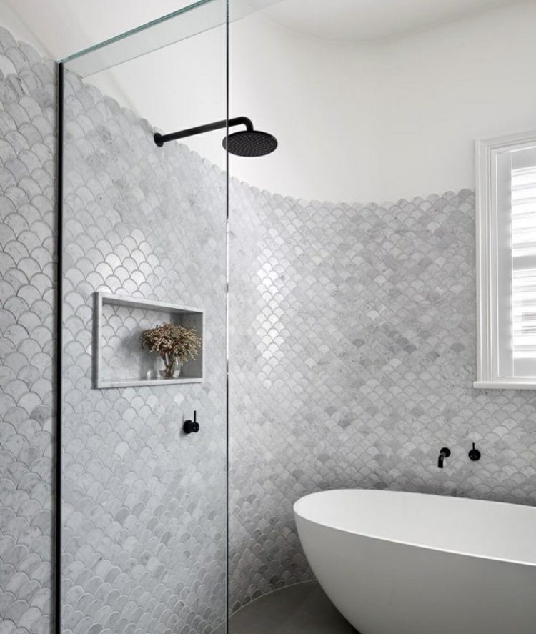 Ladrilhos de escama de peixe cinza adornam uma parede arredondada no banheiro com um chuveiro aberto