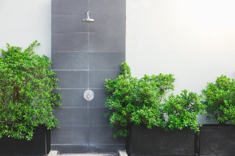 design minimalista para chuveiro ao ar livre com azulejos cinza e plantas verdes como destaque no design do jardim
