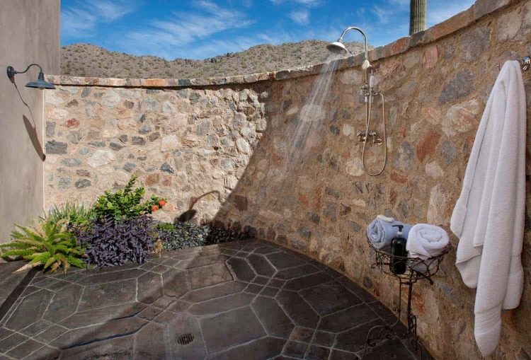parede de pedra abobadada e piso rústica na área do chuveiro com design mediterrâneo