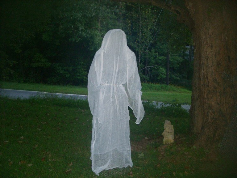 Fantasma flutuante de Halloween com manto ao lado de uma árvore