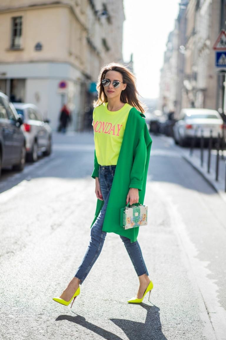 Sapatilhas de neon amarelo luminoso com uma camisa combinando, jeans azul e casaco verde