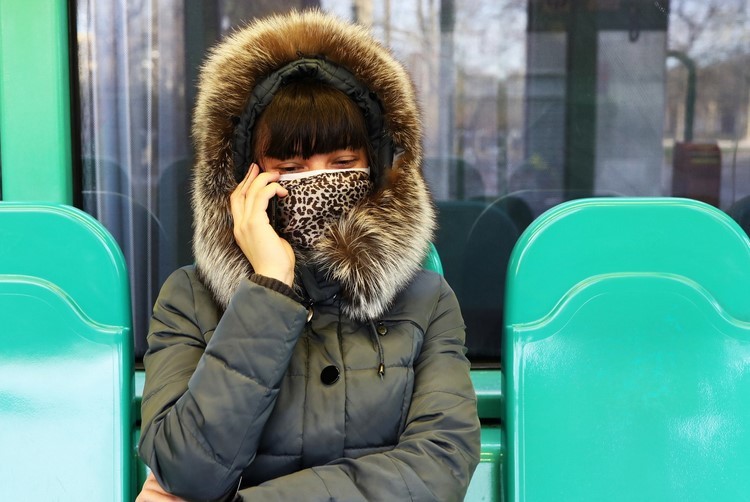 Mulher usa máscara de pano e espera no ponto de ônibus