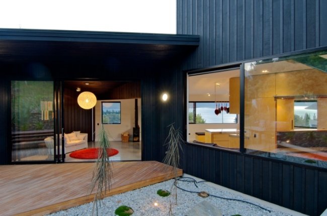 Casa com iluminação na varanda - deck de madeira porta corrediça - parede de vidro - jardim - planta
