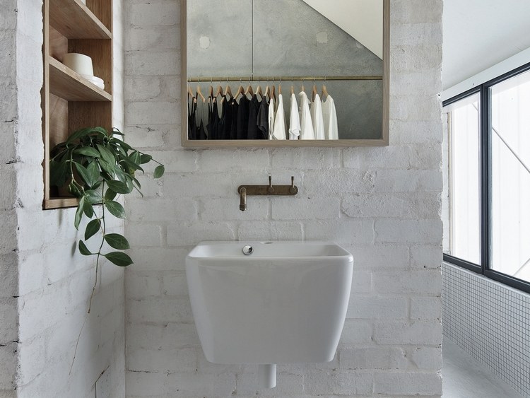 Lavatório com torneira rústica e espelho próximo ao nicho do banheiro em parede de tijolos na cor branca