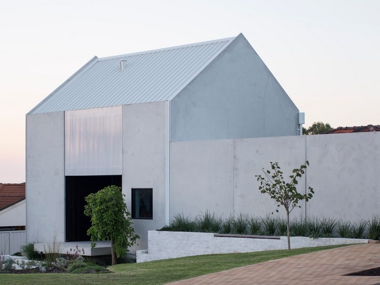 Jardim de design minimalista com gramado e árvores na frente da casa com paredes de concreto e telhado inclinado