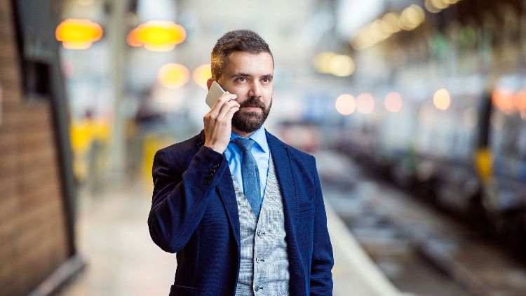 casaco azul escuro colete xadrez cinza camisa azul claro telefone celular liga para estação de trem