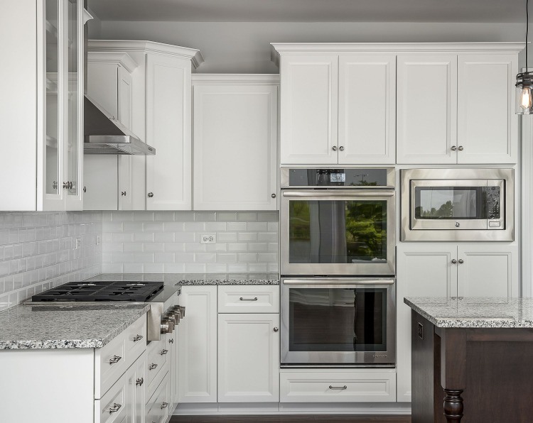 cozinha nobre com armários brancos e micro-ondas em combinação com dois fornos e placas de fogão