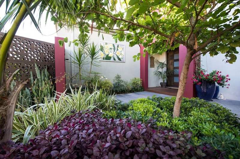 Pequeno jardim coberto com folhas vermelhas e árvores com cercas de metal perfuradas