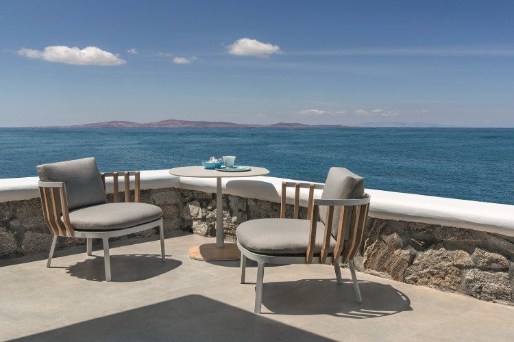 duas poltronas estofadas e mesa redonda em terraço com vista para o mar da ilha