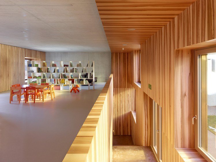 interior com painéis de madeira sala de leitura para crianças com cadeiras, mesa, janela e escada