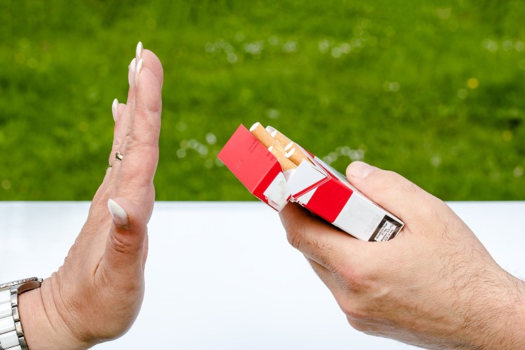 Braço feminino faz um gesto persistente em direção ao maço de cigarros ao ar livre
