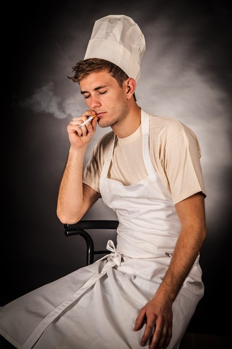 Cozinheiro com chapéu e avental branco fuma um cigarro