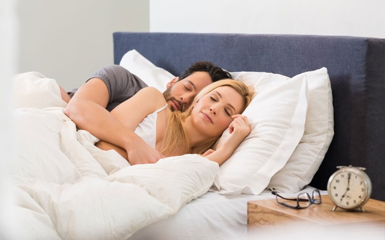 homem e mulher dormem juntos na cama com despertador e óculos na mesa de cabeceira