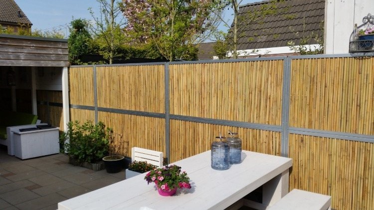 Cerca de bambu caseiro no pátio com garagem e mesa branca no verão