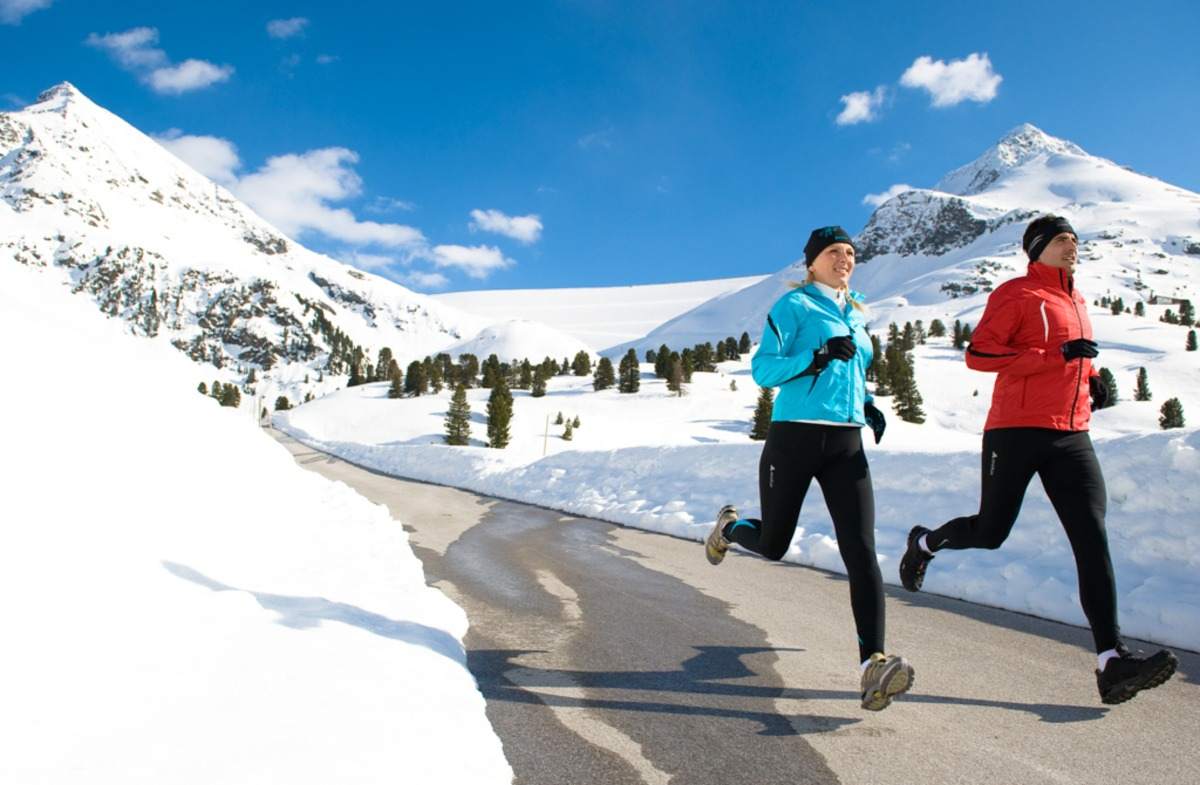 mulher e homem correm entre neve e montanhas no inverno