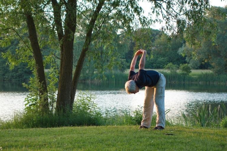 Homem idoso fazendo ioga na natureza em frente a um lago