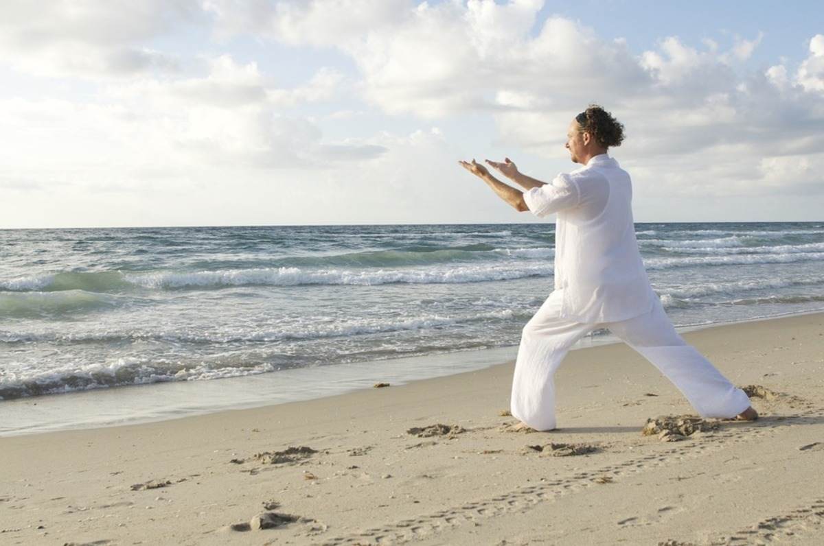 homem com roupas brancas fazendo ioga na praia