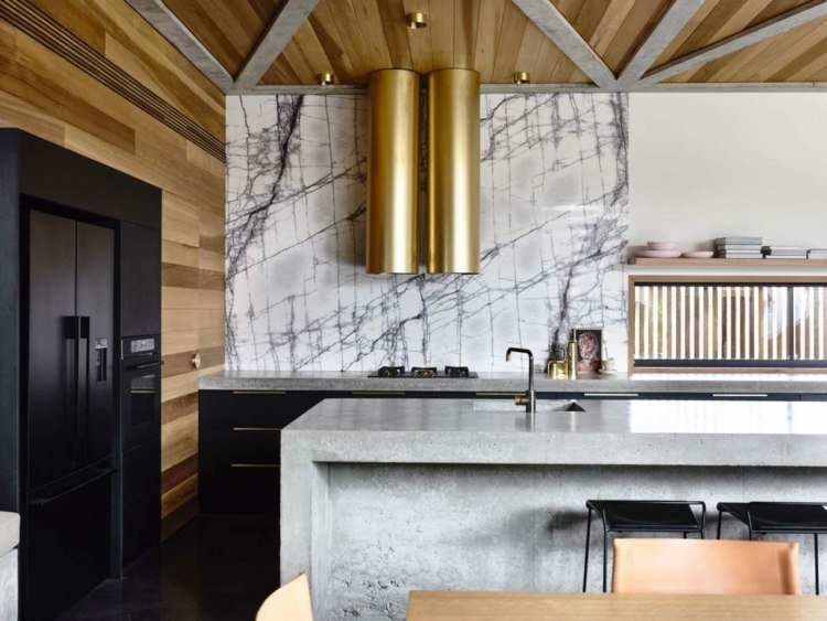 A ilha da cozinha em concreto parece combinada com armários pretos e pedra natural