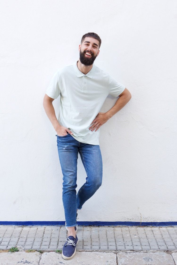 homem barbudo sorridente com camisa pólo e jeans