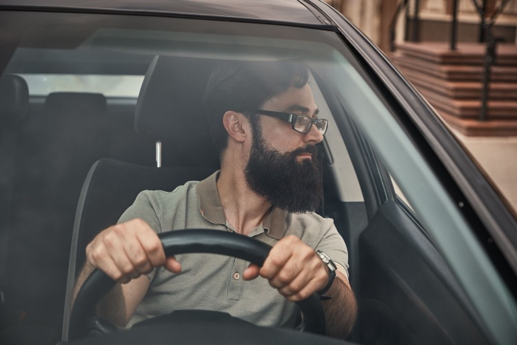 Homem de aparência moderna com barba cheia e óculos no carro